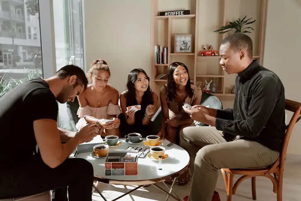 Group of friends smiling and cheering around a table with a card game
